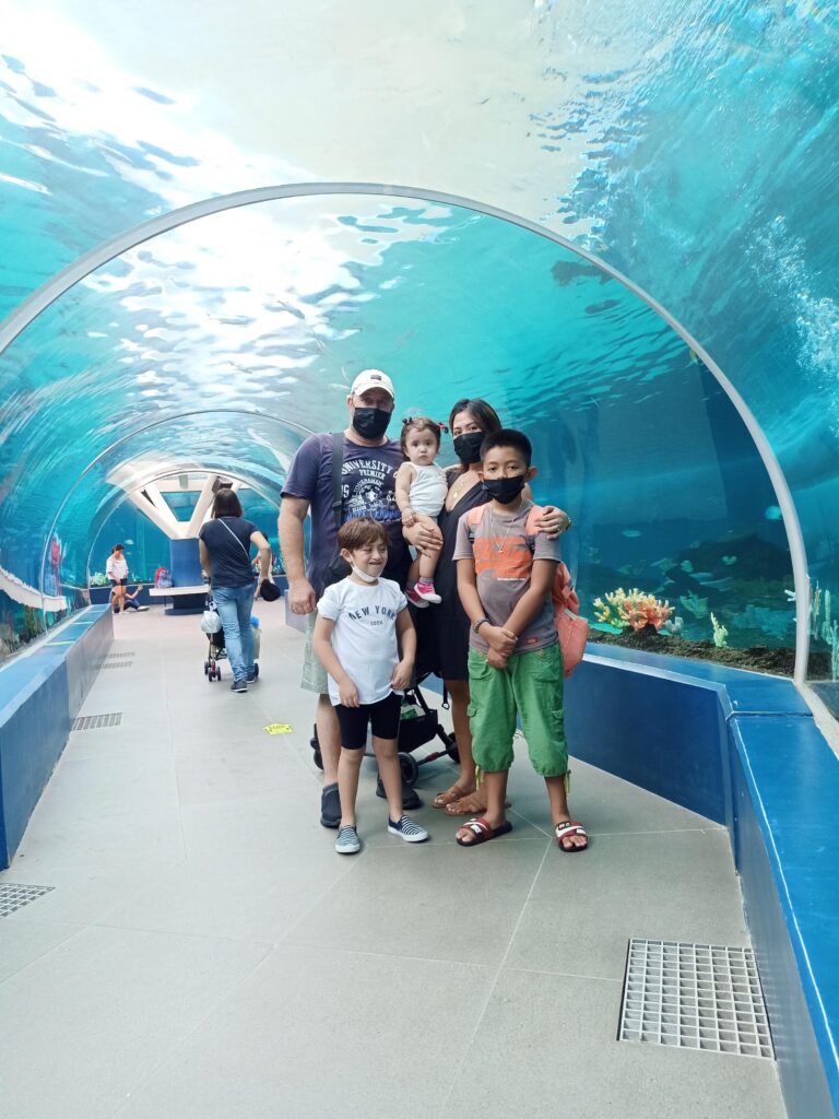 An excited family smiles and poses for photos in front of the mesmerizing backdrop of Cebu Ocean Park's main entrance, surrounded by vibrant marine-themed decorations.