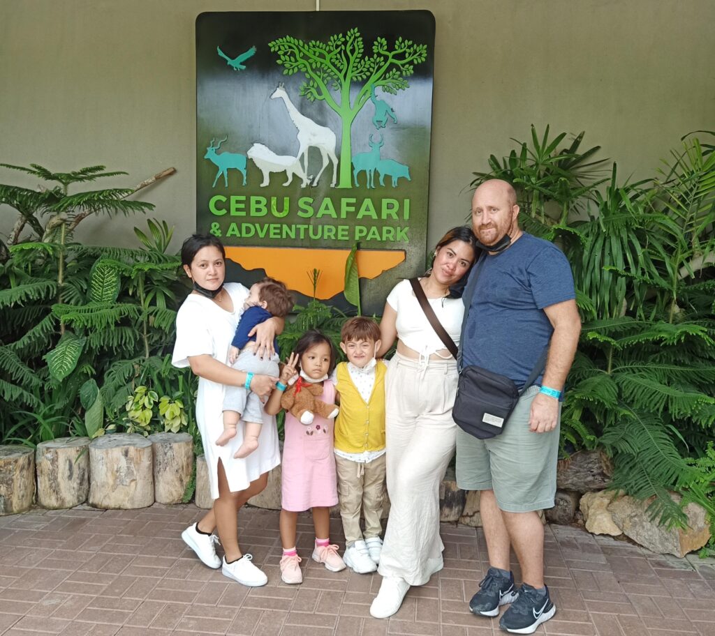 A family explores Cebu Safari and Adventure Park, enjoying the lush greenery, diverse wildlife, and exciting adventure activities. They smile for photos, ride safari vehicles, and marvel at animals like tigers, giraffes, and exotic birds.